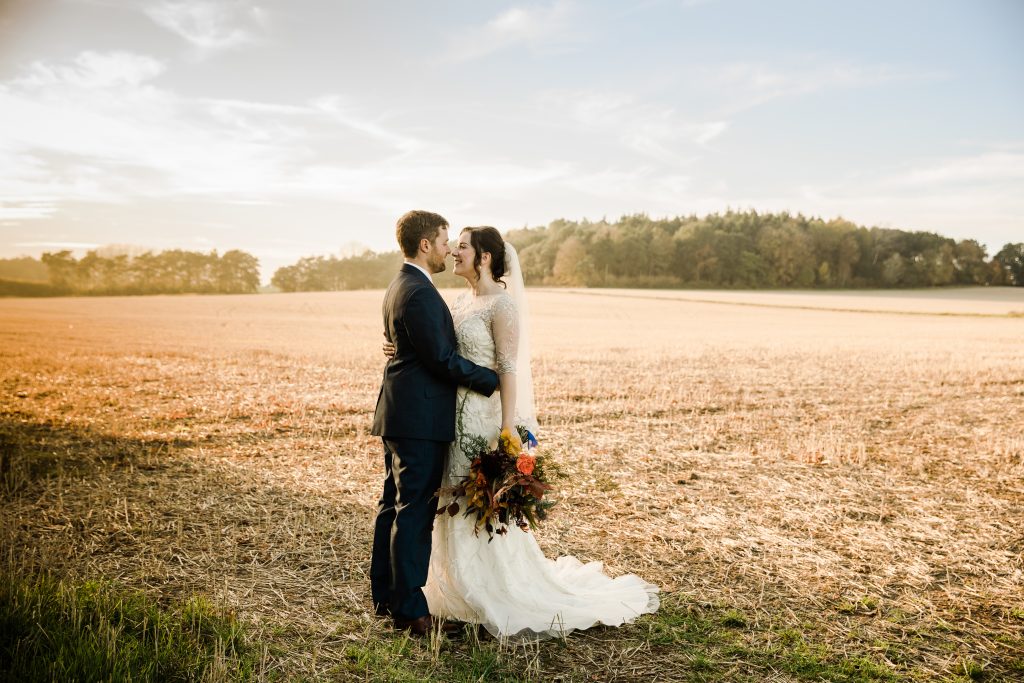 bride and groom embrace in farm field english countryside Orange & Blue Autumn Barn Wedding swallows nest barn
